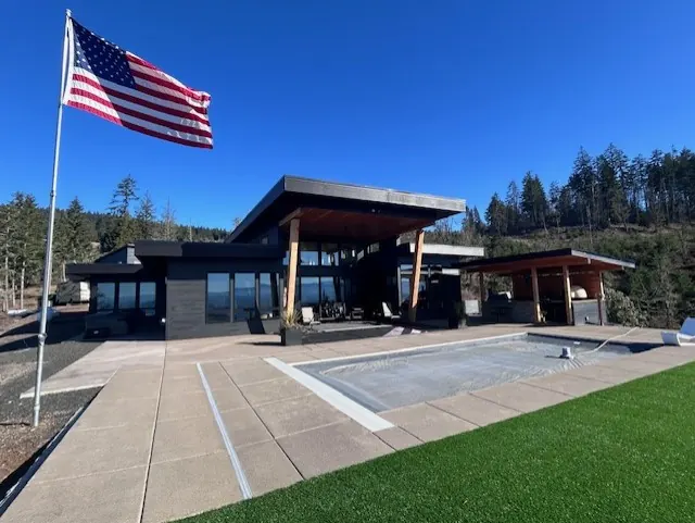 Contemporary home with dark siding beside a pool and covered patio