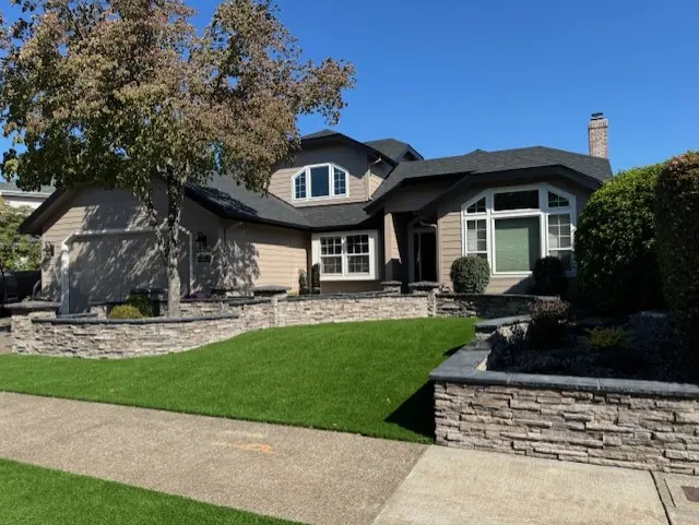 Tan two-story home with stone retaining walls and artificial turf